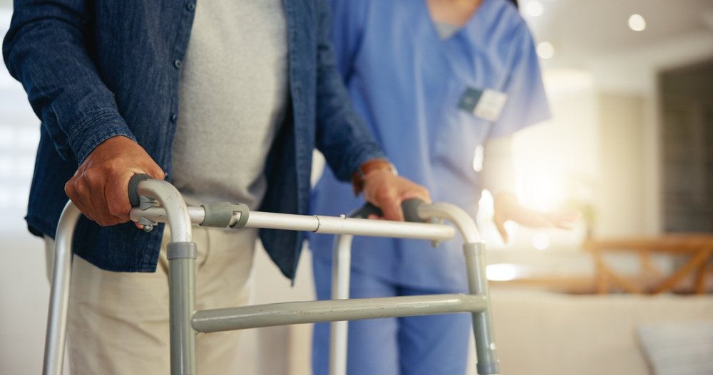 Elderly nursing home resident using a walker with assistance from a caregiver