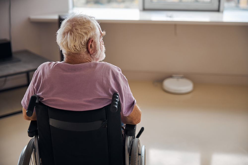 Elderly man in a wheelchair looking out a window, representing isolation, neglect, or emotional abuse in a nursing home setting