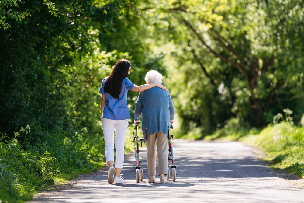 Caregiver walking beside an elderly resident using a walker outdoors, symbolizing the duty of care nursing homes owe to residents.
