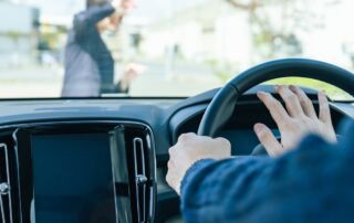 Driver in a car honking at a woman crossing the street in a crosswalk.