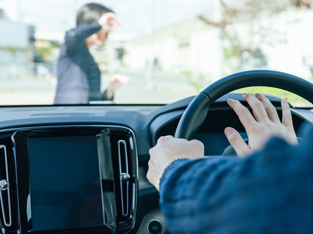Driver in a car honking at a woman crossing the street in a crosswalk.