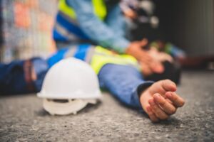 A person wearing a hard hat is lying on the ground, illustrating a fall on a construction site.