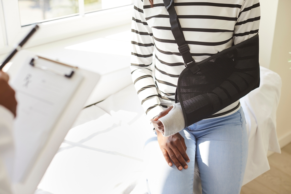 Seeking medical treatment after an acciden Injured person with their arm in a sling speaking with a doctor, highlighting the need for prompt medical treatment after an accident.