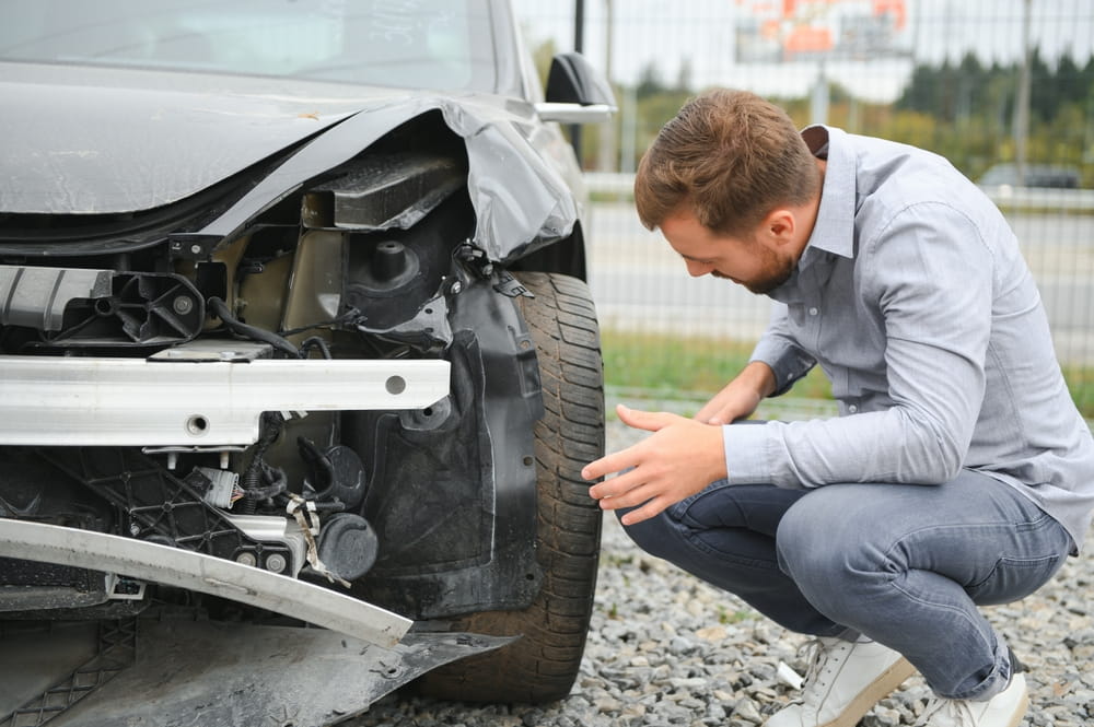 Driver inspecting vehicle damage after a car accident while reviewing insurance claim options in Indiana